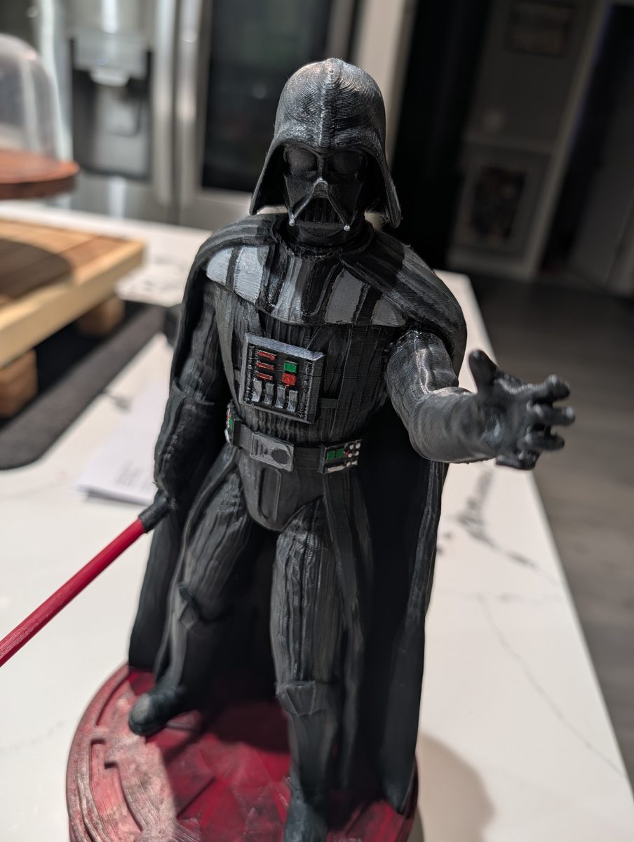 A hand-painted 3D-printed Darth Vader with a red lightsaber, standing on a red floating tree platform