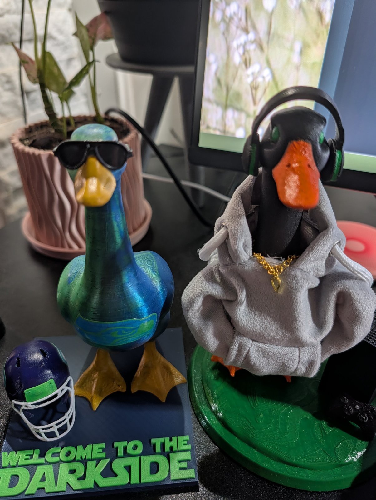 Two geese dressed up: one in a grey hoodie with a gold chain and headset, one in sunglasses